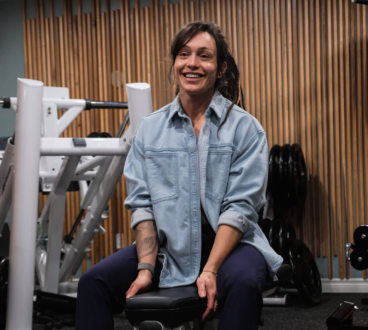 Jess Zawadowicz, founder of Bar None Fitness Studio, seated in the studio in front of the wood slat wall